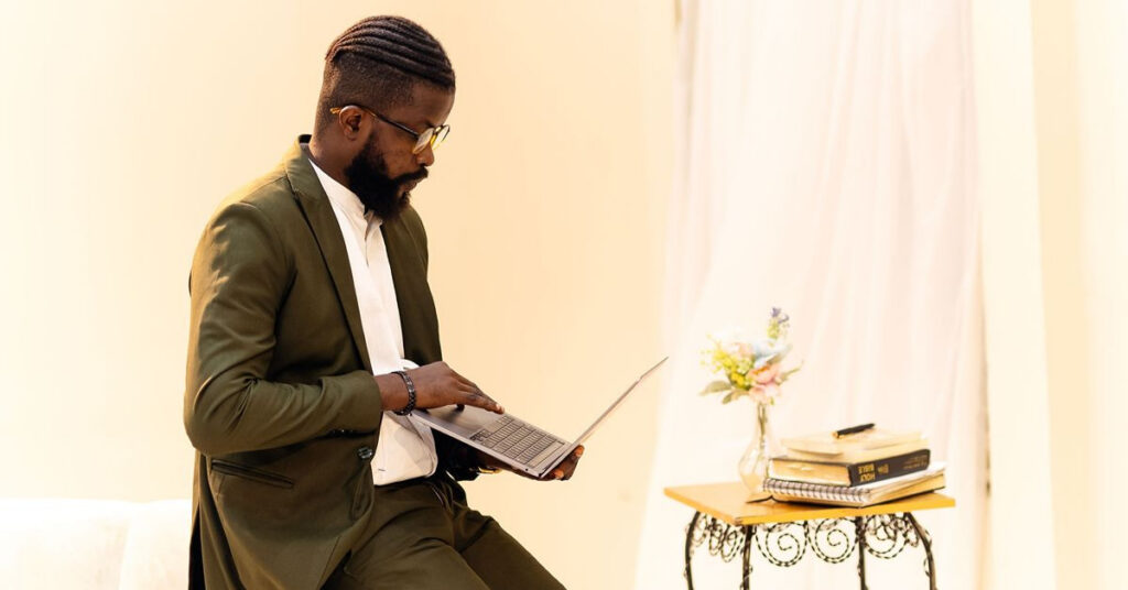 Man wearing an olive green suit while working on a laptop.