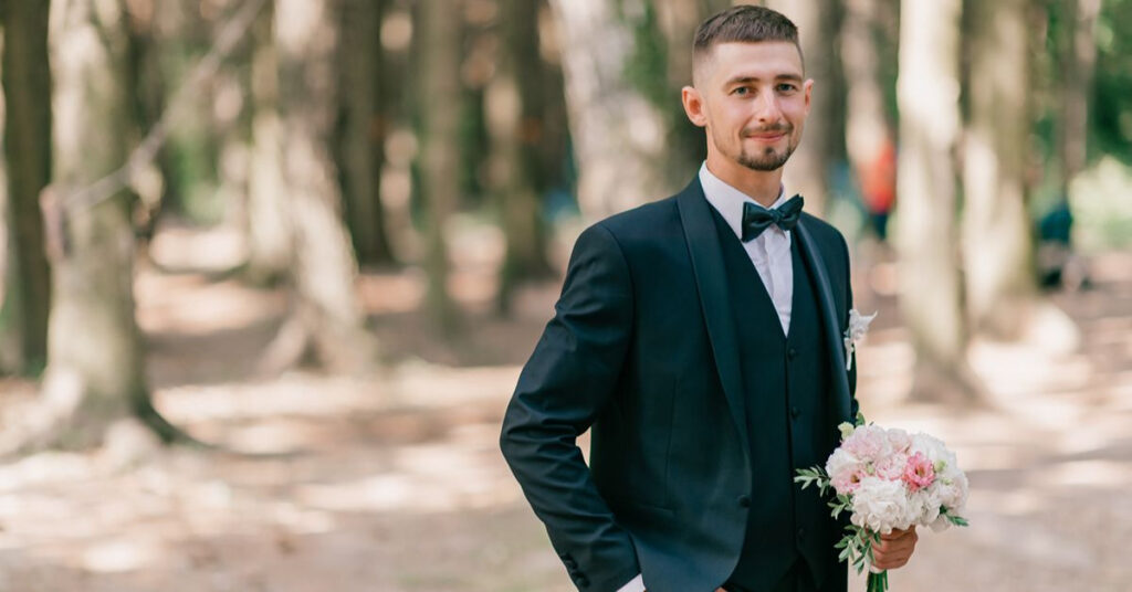 Groom wearing a dark green suit and bow tie outdoors.