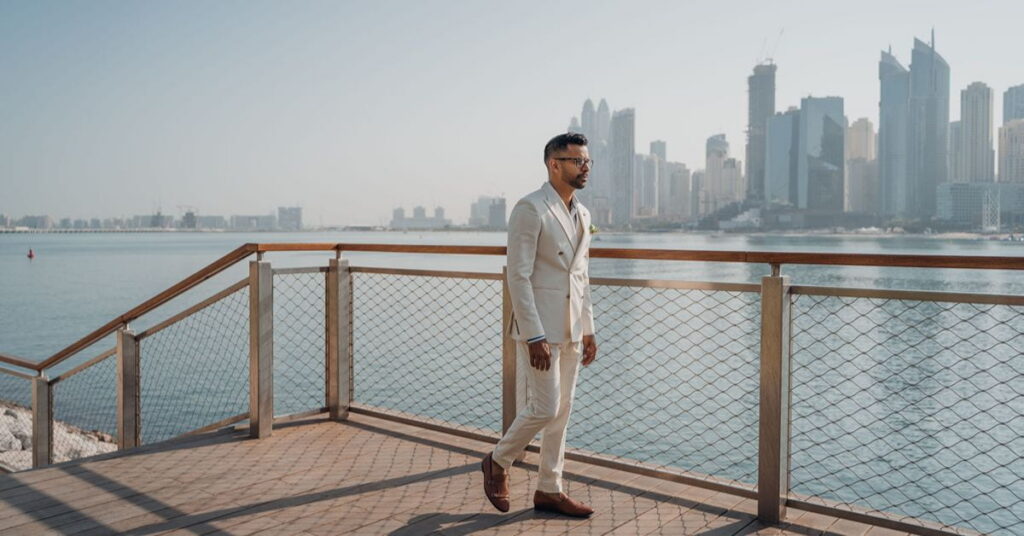 Man in ivory suit by waterfront with city skyline