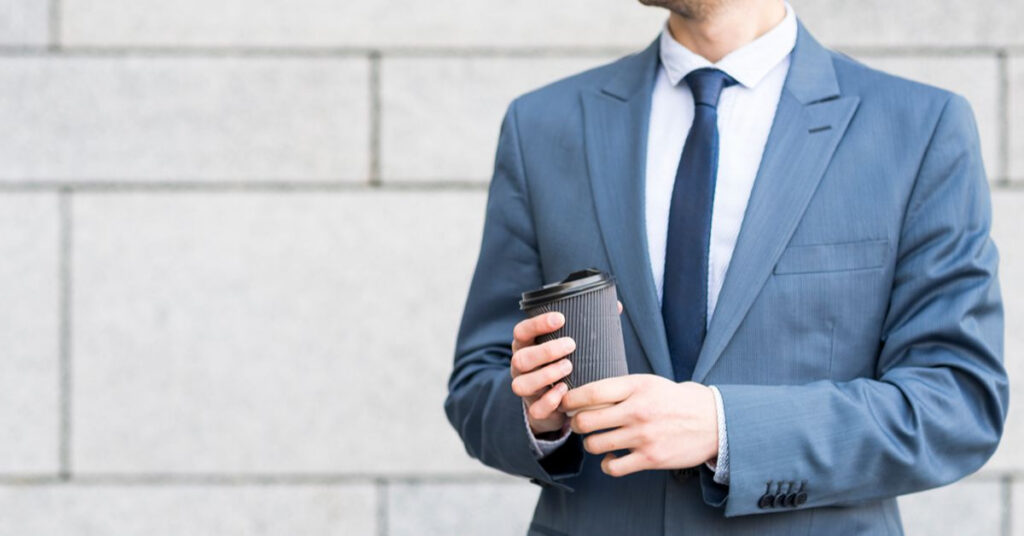 Man in slate blue suit holding coffee cup
