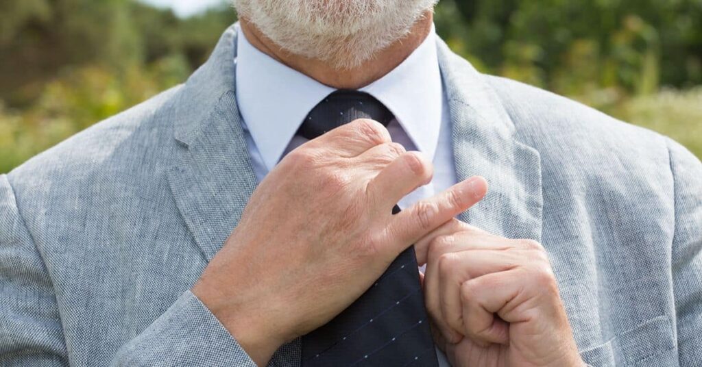 Man adjusting a light grey suit and navy tie outdoors
