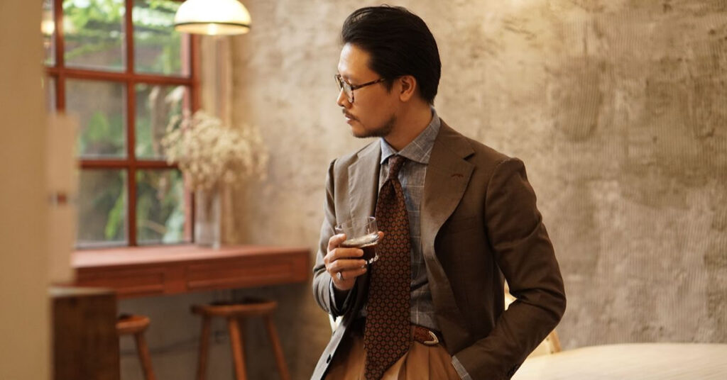 Man wearing a brown suit with a patterned shirt and tie.